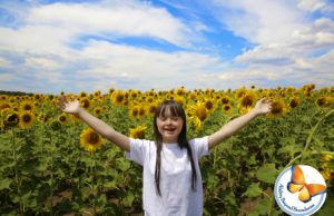 A girl at a sunflower farm has her hands raised and is smiling